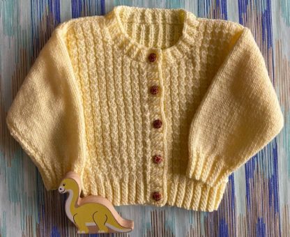 Hand knitted endearing patterned cardigan in a soft yellow Round neck 5 Delightful buttons in front Long sleeves Ribbing around neckline, cuffs and hem 100% Acrylic yarn Completed garment measurements Chest all around: 55cm Length, shoulder to hem ribbing: 28cm Sleeve seam length: 21cm