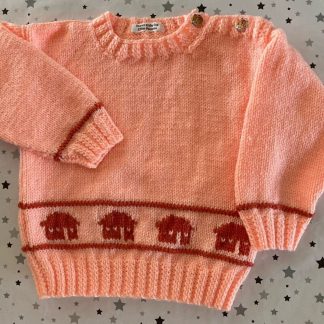 Hand knitted peach jumper with house motifs Round neck 3 Whimsical elephant buttons on one shoulder Long sleeves Ribbing around neckline, cuffs and hem 100% Acrylic yarn Completed garment measurements Chest all around: 62cm Length, shoulder to hem ribbing: 31cm Sleeve seam length: 24cm For ages 12-18 months