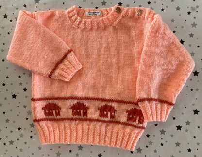 Hand knitted peach jumper with house motifs Round neck 3 Whimsical elephant buttons on one shoulder Long sleeves Ribbing around neckline, cuffs and hem 100% Acrylic yarn Completed garment measurements Chest all around: 62cm Length, shoulder to hem ribbing: 31cm Sleeve seam length: 24cm For ages 12-18 months